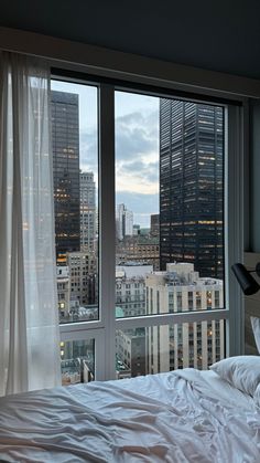 a bedroom with a large window overlooking the city at night, and white linens on the bed