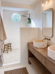 two sinks in a bathroom under a large mirror and lights above the sink is a stool with a plant on it