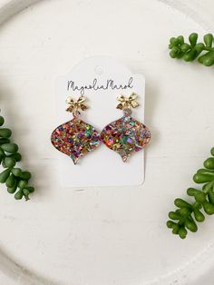 "This listing is for one pair of Christmas ornament bauble earrings in a merry and bright rainbow glittered acrylic completed with gold bow studs. These are only available in limited quantities. Due to the handmade nature of this item, pattern placement may vary. Acrylic Glitter Ornament Baubles Approximate size: 1.75\" Are you new to cork and leather(and now acrylic) earrings? They are lightweight, the perfect accessory to ANY outfit and highly addicting! Need a different color? We are happy to create a custom pair for you!                    *THANK YOU SO MUCH* Thank you for shopping with Magnolia Marsh. We look forward to creating something special and unique for you. If you have questions or need a custom order please message us! Please share and tag Magnolia Marsh in your pictures in Gold Earrings For Party And Holiday, Gold Holiday Earrings For Party, Whimsical Dangle Earrings For Party, Whimsical Drop Earrings For Party, Multicolor Earrings For Holiday Gifts, Silver Earrings For Holiday Parties, Holiday Multicolor Earrings Perfect For Gifts, Holiday Multicolor Earrings As Gift, Sparkling Jewelry For Christmas Party