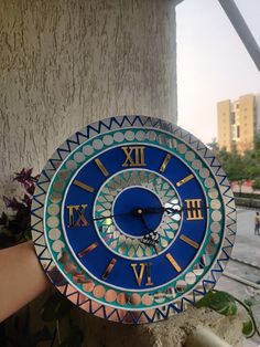 a blue and white clock with roman numerals is held up by someone's hand