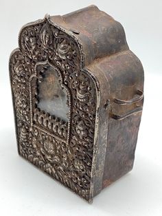 an old metal box with ornate carvings on the front and sides, sitting on a white surface