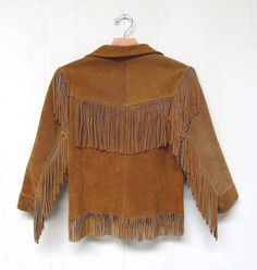 * Fringed western style jacket c 1950s* Caramel brown rough-out suede* Double hip pockets* Long, set-in sleeves * Open collar with 3 metal snap front closure* Fully lined in a great brown and white calico pattern rayon fabricLabel: Jo-o-KayVery good condition. A single fringe is missing in front. Lining is torn at the shoulder seams (see last image)Approximate US size: 16Chest: 34Shoulder: 14Sleeve: 18 Length: 22Garments are flat-measured. Please compare these measurements to another flat-measur Retro Long Sleeve Outerwear For Rodeo, American Retro Long Sleeve Outerwear For Fall, Vintage Long Sleeve Outerwear For Rodeo, Vintage Fringed Winter Outerwear, Vintage Fringe Outerwear For Winter, Vintage Winter Outerwear With Fringe, Vintage Fall Outerwear For Ranch, Vintage Fitted Outerwear With Fringe, Fitted Vintage Outerwear With Fringe