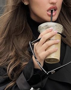 a woman with long hair drinking from a plastic cup and holding a straw in her hand