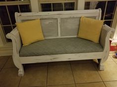 a white wooden bench with yellow pillows on it's seat and windows in the background