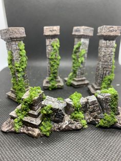 some moss covered rocks and pillars on top of a black surface with white walls in the background