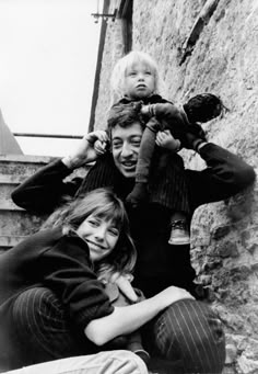 a black and white photo of two people with a child on their shoulders, sitting next to each other