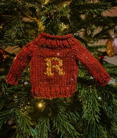 a red knitted sweater hanging from a christmas tree with ornaments on the branches around it