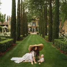 a woman sitting on the ground with a baby in front of her and an enormous hat over her head