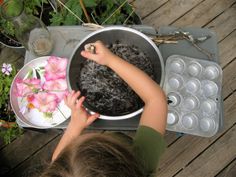 a young boy is playing with some flowers in a bowl and muffin tins