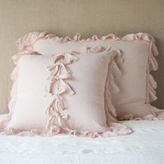 three pink pillows with ruffled edges sit on a white pillowcase in front of a beige headboard