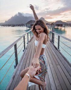 two people are holding hands on a pier near the water and some huts in the background