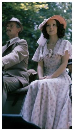 a woman in a dress and hat sitting next to a man on a horse drawn carriage