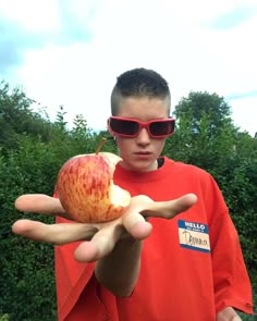 a boy wearing sunglasses holding an apple in his hand with the palm of his hand