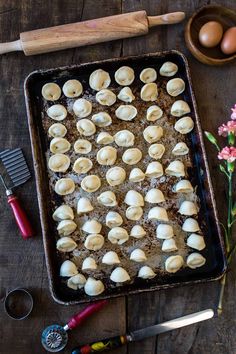 a baking pan filled with dumplings on top of a wooden table next to utensils