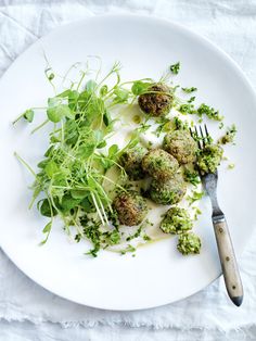 a white plate topped with broccoli and meatballs covered in sauce next to a fork