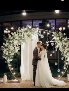 a bride and groom kissing in front of an arch decorated with flowers, candles and bubbles