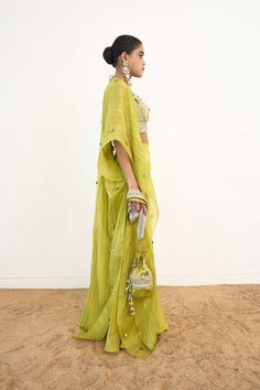 Introducing a captivating lime green cape set, exuding elegance and sophistication. The eye-catching cape is crafted with finesse from organza, taffeta, and chanderi silk, featuring intricate trim, delicate cutwork, and exquisite hand embroidery. Paired with a chic bralette and pants, this ensemble is perfect for making a stylish statement at any occasion. Green Cape, Cape Set, Cut Work, Pant Set, Green Fabric, Lime Green, Occasion Wear, Hand Embroidery, Bralette