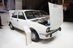 an old white car with its hood open on display in a museum exhibit area,