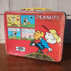 an old tin lunch box with peanuts cartoon on the front and side, sitting on a wooden table