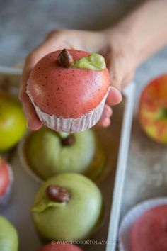 a person holding an apple in front of some cupcakes