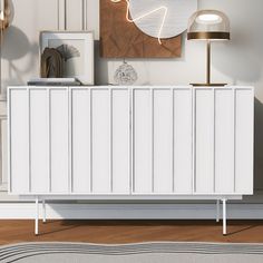 a white cabinet sitting on top of a wooden floor next to a lamp and pictures