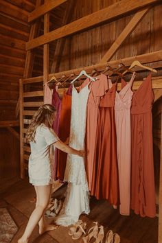 a woman is looking at dresses hanging on a rack in a room with wooden walls