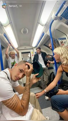 a group of people sitting on a train next to each other and one person holding a hat