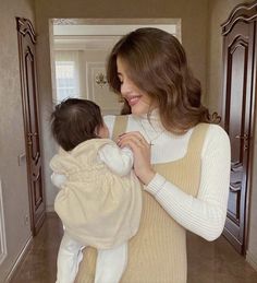 a woman holding a baby wrapped in a blanket while standing next to a door way