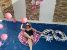 a woman sitting on an inflatable pool float with balloons floating around her,