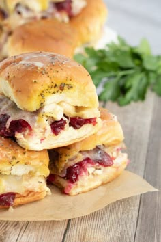 several sandwiches stacked on top of each other with cranberry sauce and herbs in the background