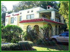 a car parked in front of a yellow house with red roof and green shutters