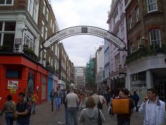 many people are walking down the street in front of shops and buildings with an arched sign above them