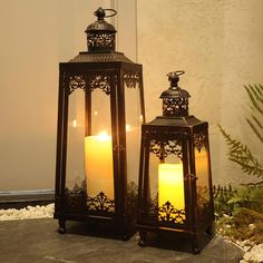 two lit candles sitting next to each other on top of a stone slab in front of a building