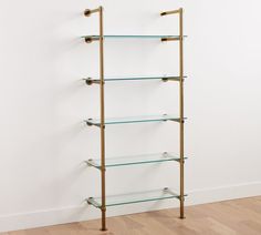 a gold shelf with glass shelves on the bottom and brass handles, against a white wall