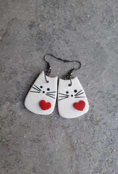 pair of cat shaped ceramic earrings with red heart eyes on concrete surface, closeup