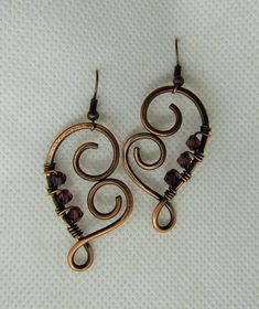 two pairs of earrings are shown on a white surface, one is shaped like a heart and the other has an intricate design