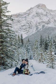 a bride and groom are sitting in the snow on their wedding day with mountains in the background