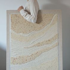 a man sitting on top of a large piece of knitted art with his hands in the air