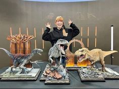 a woman is standing in front of some dinosaur figurines on a table with their hands up