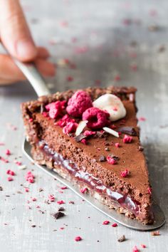 a piece of chocolate cake with raspberries and whipped cream on top is being held by a fork