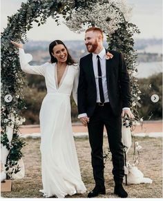 a bride and groom standing under an arch with greenery on the side holding hands