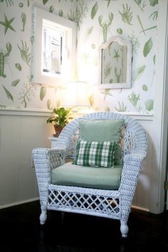 a white wicker chair sitting in front of a wall with green and white wallpaper