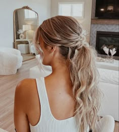 a woman with long hair sitting in front of a mirror wearing a white top and ponytail