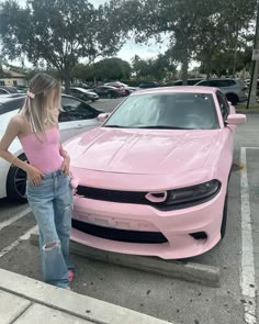 a woman standing next to a pink car in a parking lot