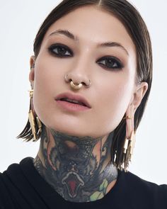 a woman with tattoos and piercings on her face is looking at the camera while wearing large gold hoop earrings