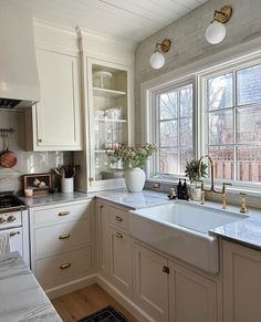 a white kitchen with marble counter tops and gold faucets on the windowsill