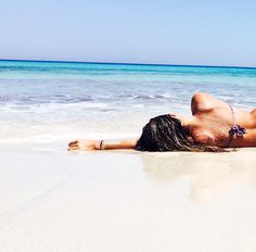 a woman laying on top of a sandy beach next to the ocean