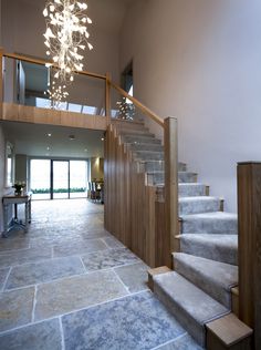 a staircase leading up to an open floor plan with glass railing and chandelier