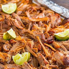 shredded pulled pork with limes and cilantro garnish in a tin foil pan