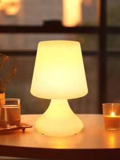 a white lamp sitting on top of a table next to a vase and two candles